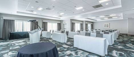 Un salón de conferencias con un escenario, filas de mesas y suelo alfombrado.