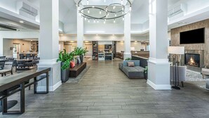 A spacious lobby with a high ceiling, a central chandelier, seating areas, a fireplace, and a large TV screen.