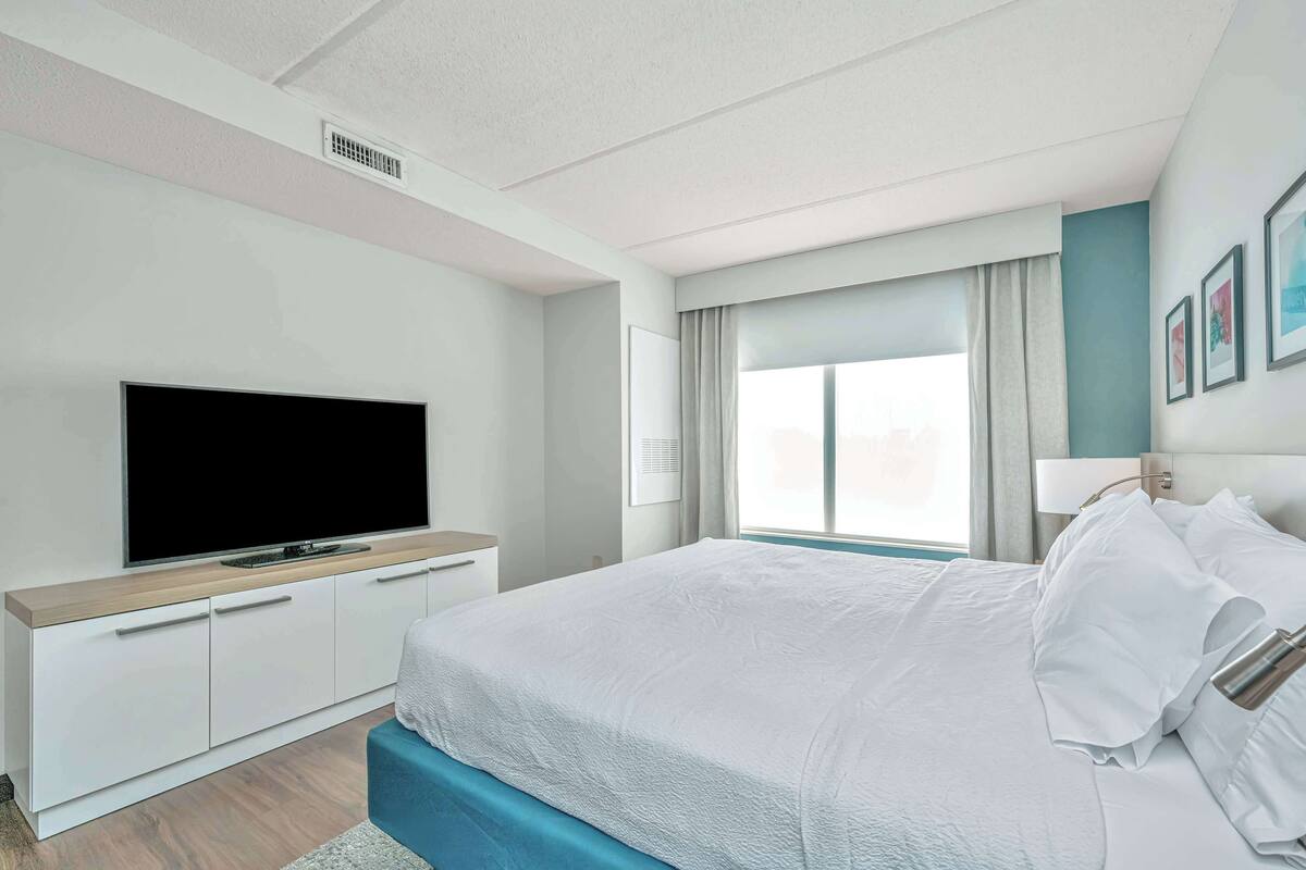 Une chambre d’hôtel moderne dotée d’un grand lit, d’une télévision à écran plat, d’une table de chevet et d’une fenêtre avec des rideaux.