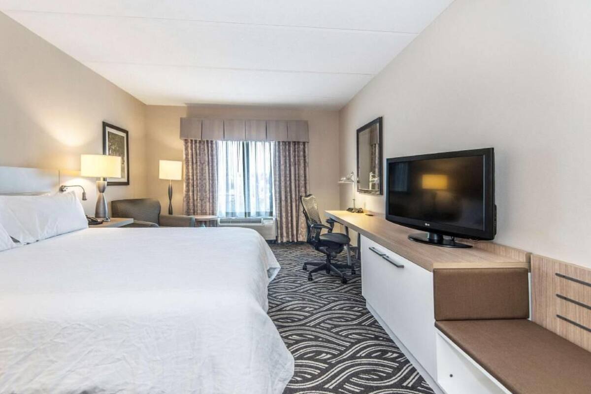 A hotel room with a bed, desk, chair, television, and a window with curtains.