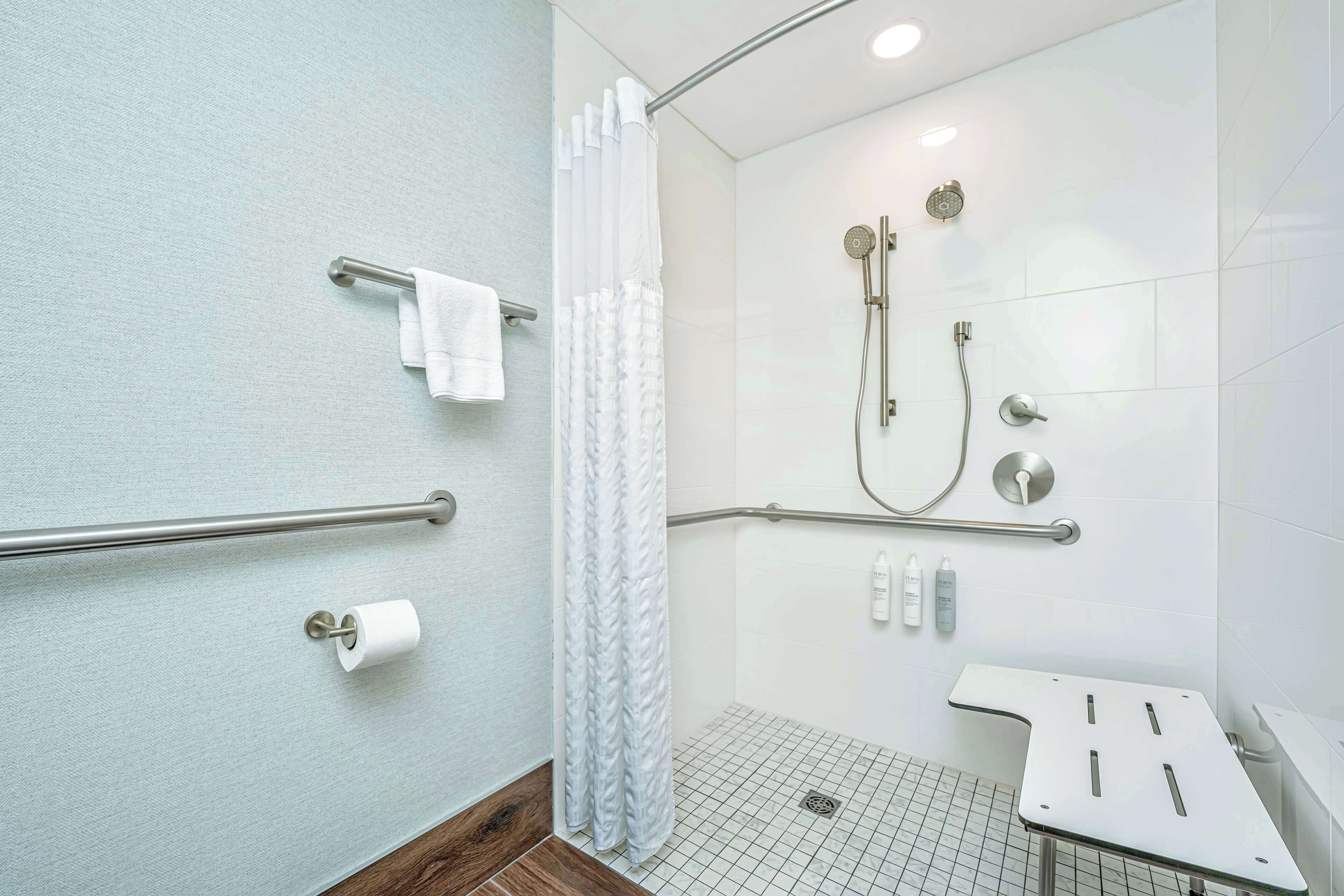 A modern bathroom with a shower, grab bars, a toilet paper holder, and a sink.