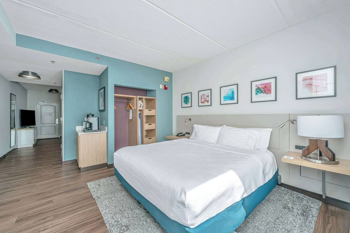 Une chambre d’hôtel moderne, dotée d’un grand lit, d’un bureau, d’une armoire et d’une salle de bain visible à travers une porte ouverte.