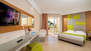 Habitación de hotel con cama, escritorio con espejo, televisor, balcón con vistas y ventana con cortinas.