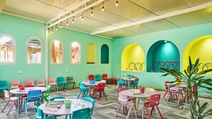 Un espacio interior luminoso y colorido con varias mesas y sillas, que ofrece diferentes disposiciones de asientos y una planta grande en maceta.
