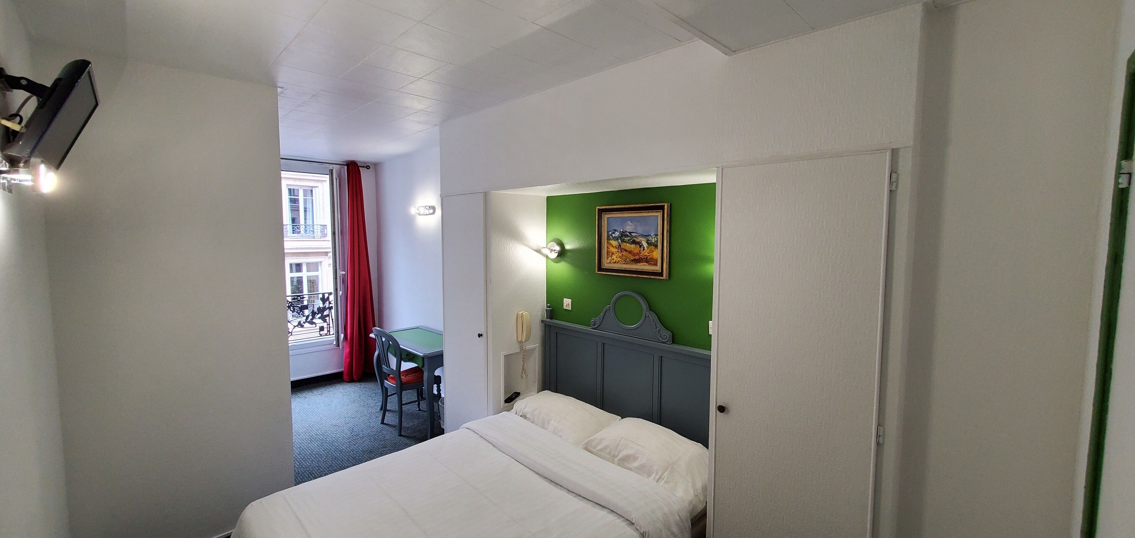 Une chambre d’hôtel avec un lit, un bureau, une chaise, un téléphone et un tableau au mur.