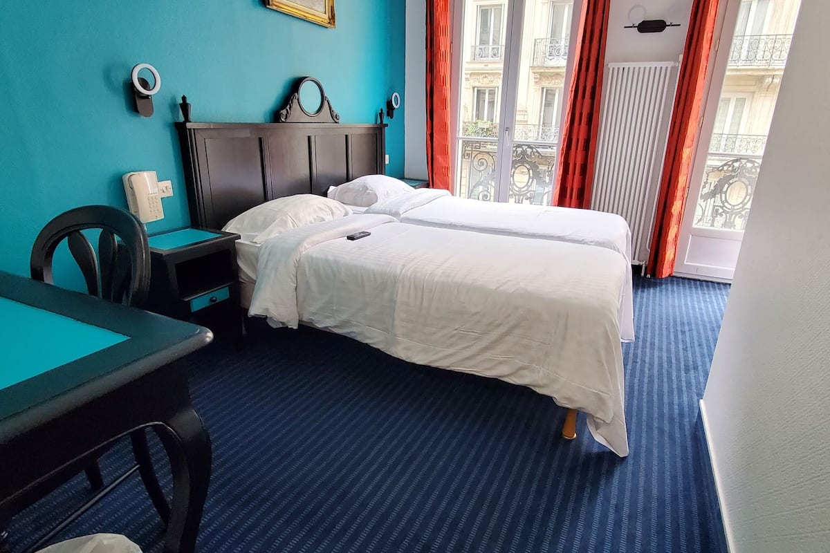 Quarto de hotel com duas camas, uma mesa de trabalho e vista para a cidade.