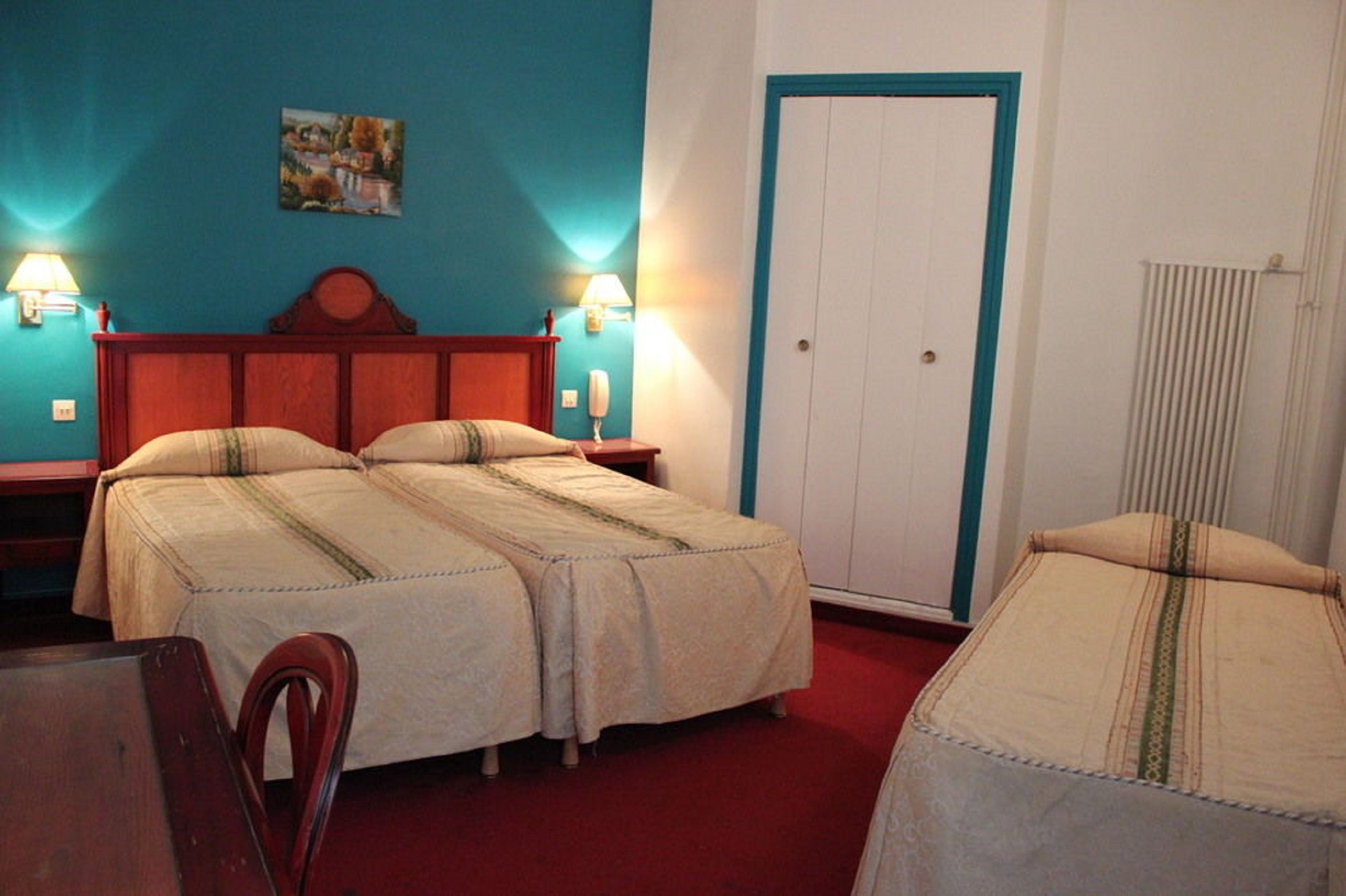 A double bed with a wooden headboard, two bedside tables with lamps, a red carpet, and a white door with a blue frame.