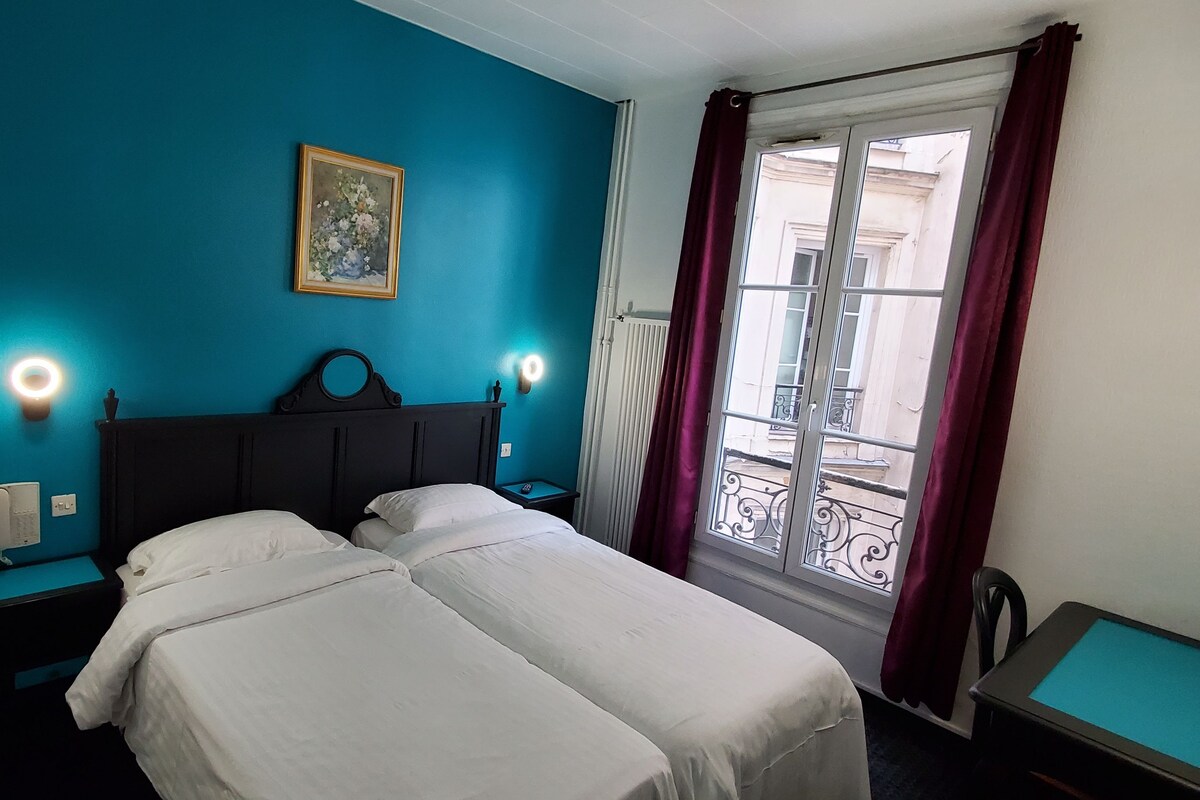 Habitación de hotel con cama, mesita de noche, cortinas y vistas al exterior.