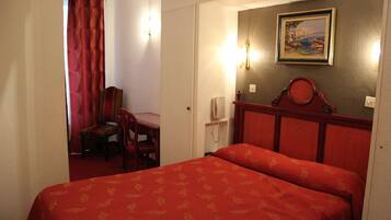 A hotel room with a bed, a chair, a desk, and a painting on the wall.