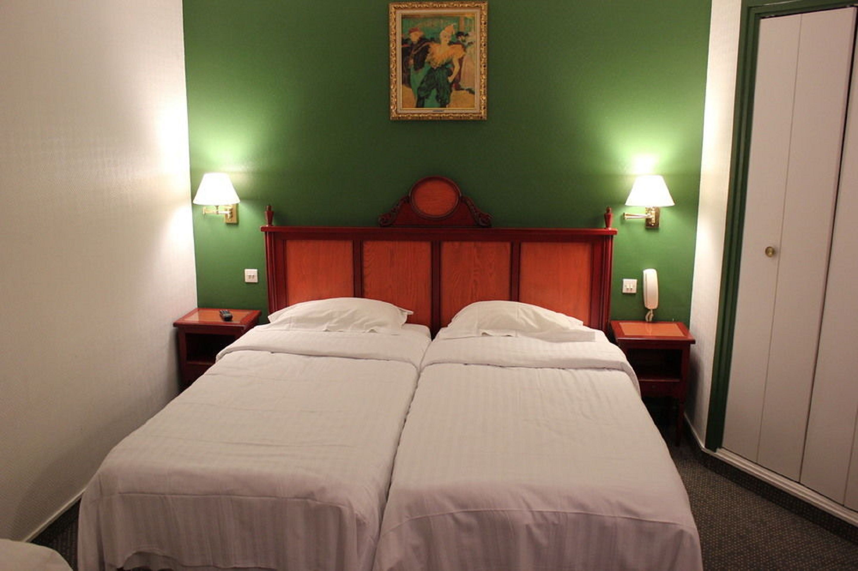 A double room with two beds, a wooden headboard, bedside lamps, and a painting on the wall.