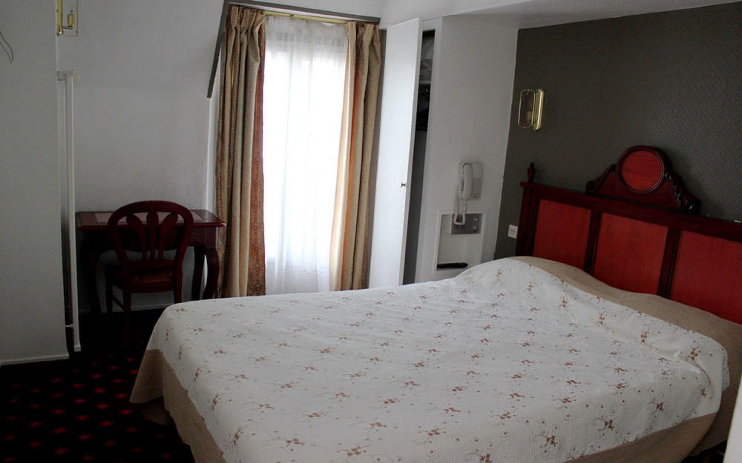A hotel room with a bed, a desk, a chair, and a wardrobe.