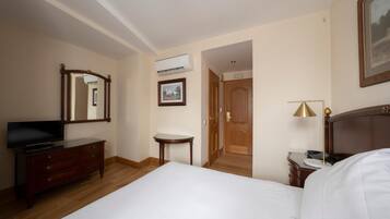 A hotel room with a bed, dresser, television, bedside table, lamp, and an air conditioning unit.