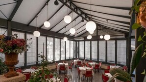 Un restaurante con techo alto, ventanas amplias y esferas colgantes como iluminación. Las mesas están dispuestas en un espacio amplio.