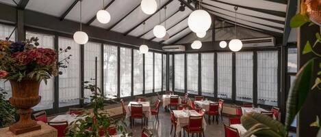 Un restaurante con techo alto, ventanas amplias y esferas colgantes como iluminación. Las mesas están dispuestas en un espacio amplio.