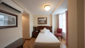 Une chambre d’hôtel avec un lit, une table de chevet, une lampe, une chaise et un tableau encadré au mur.