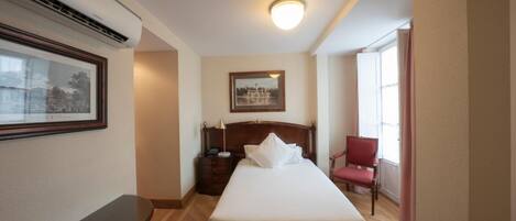 Habitación de hotel con cama, mesita de noche, lámpara, sillón y un cuadro en la pared.