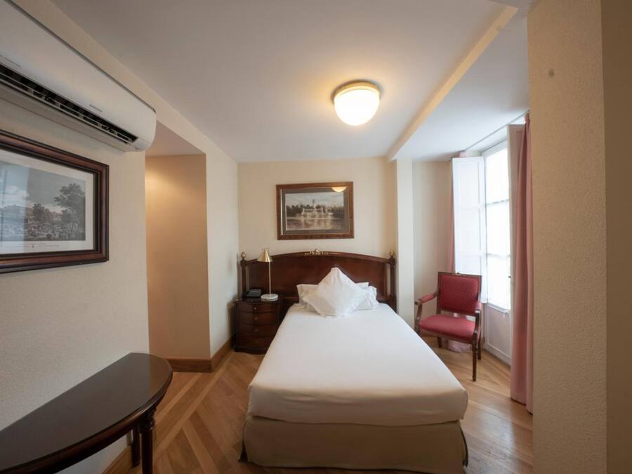 Une chambre d’hôtel avec un lit, une table de chevet, une lampe, une chaise et un tableau encadré au mur.