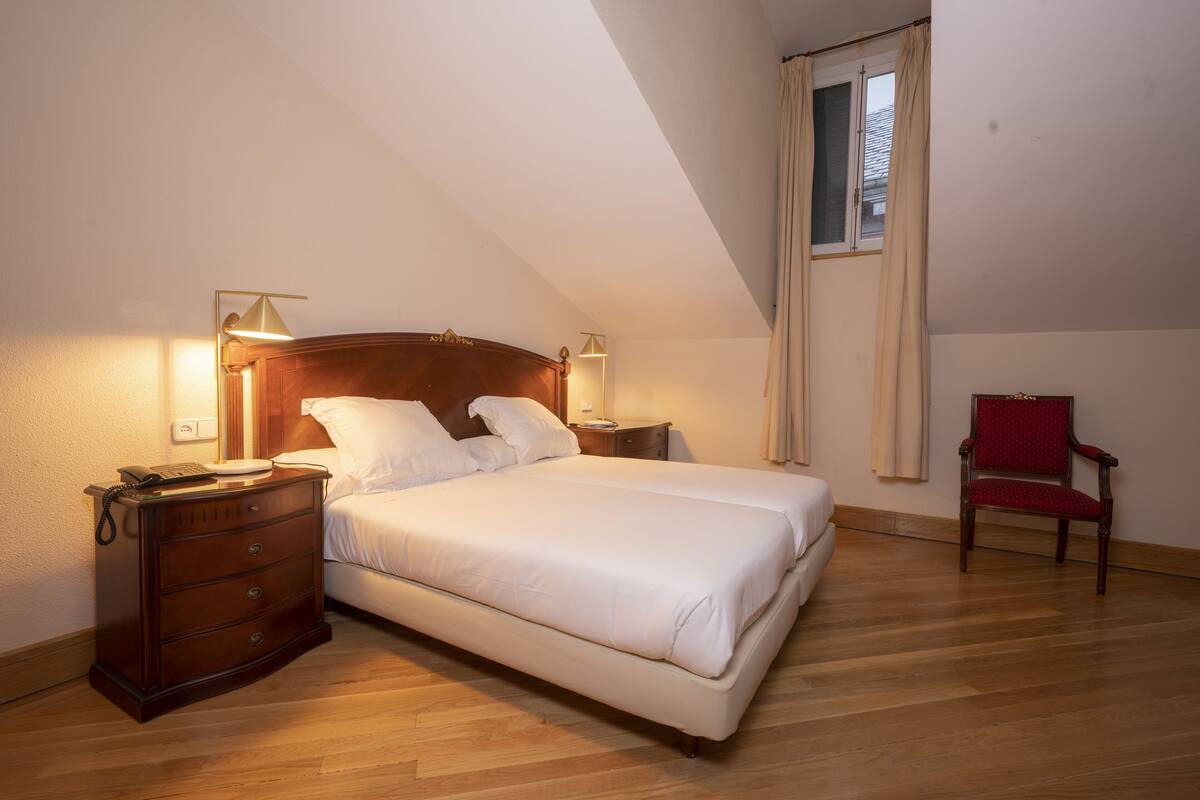 Un dormitorio con cama de madera, lámparas de noche, cómoda y ventana con cortinas.