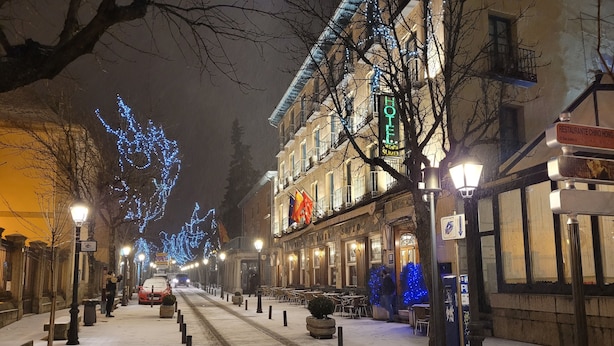 Un hotel con fachada clásica europea, mesas al aire libre y una calle cubierta de nieve.