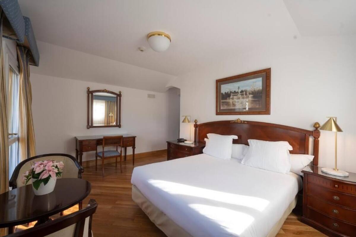 Habitación de hotel con una cama grande, un escritorio, una silla, una mesita de noche y un cuadro en la pared.