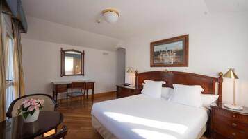 Habitación de hotel con una cama grande, un escritorio, una silla, una mesita de noche y un cuadro en la pared.
