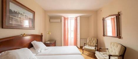 Una habitación de hotel con dos camas, una zona de estar con sillas, un cuadro en la pared y una ventana con cortinas.