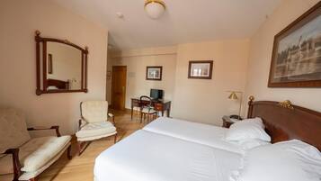 Ein Hotelzimmer mit einem großen Bett, zwei Sesseln, einem Schreibtisch mit Computer und einem Spiegel an der Wand.