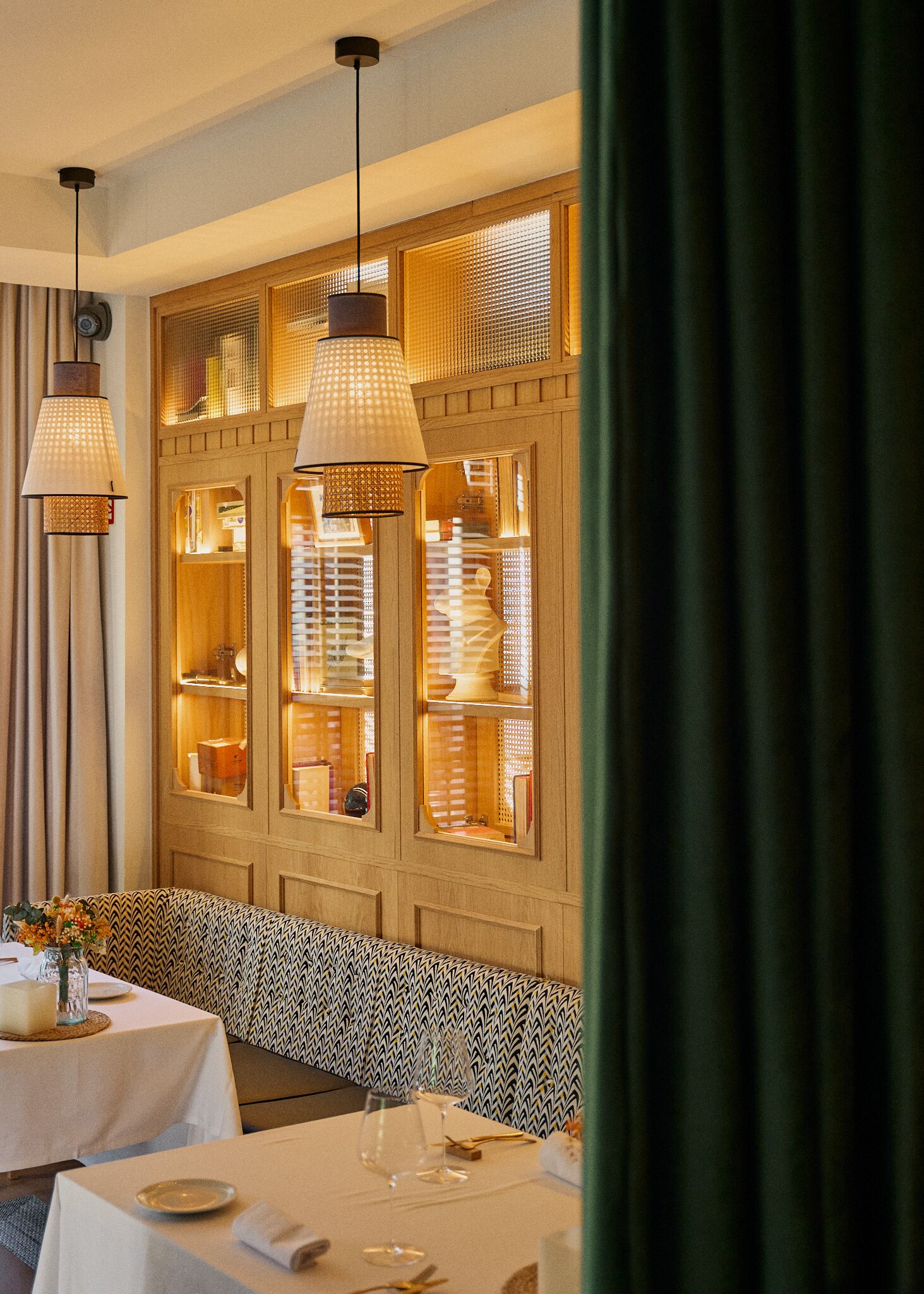 A dining area with a wooden panel wall, hanging pendant lights, and a bench.
