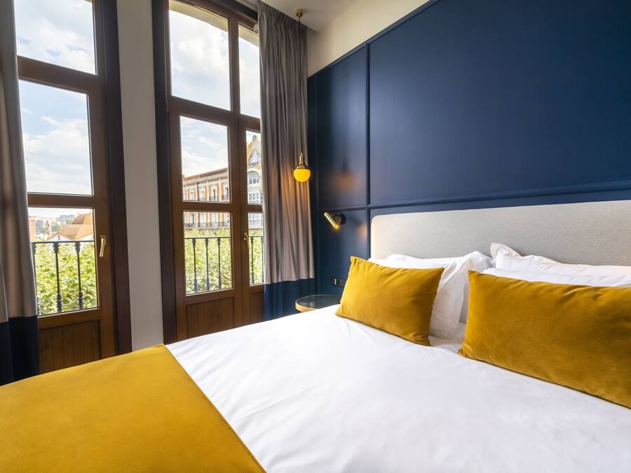 Habitación de hotel con una cama grande, dos almohadas, una mesita de noche y una ventana con cortinas.