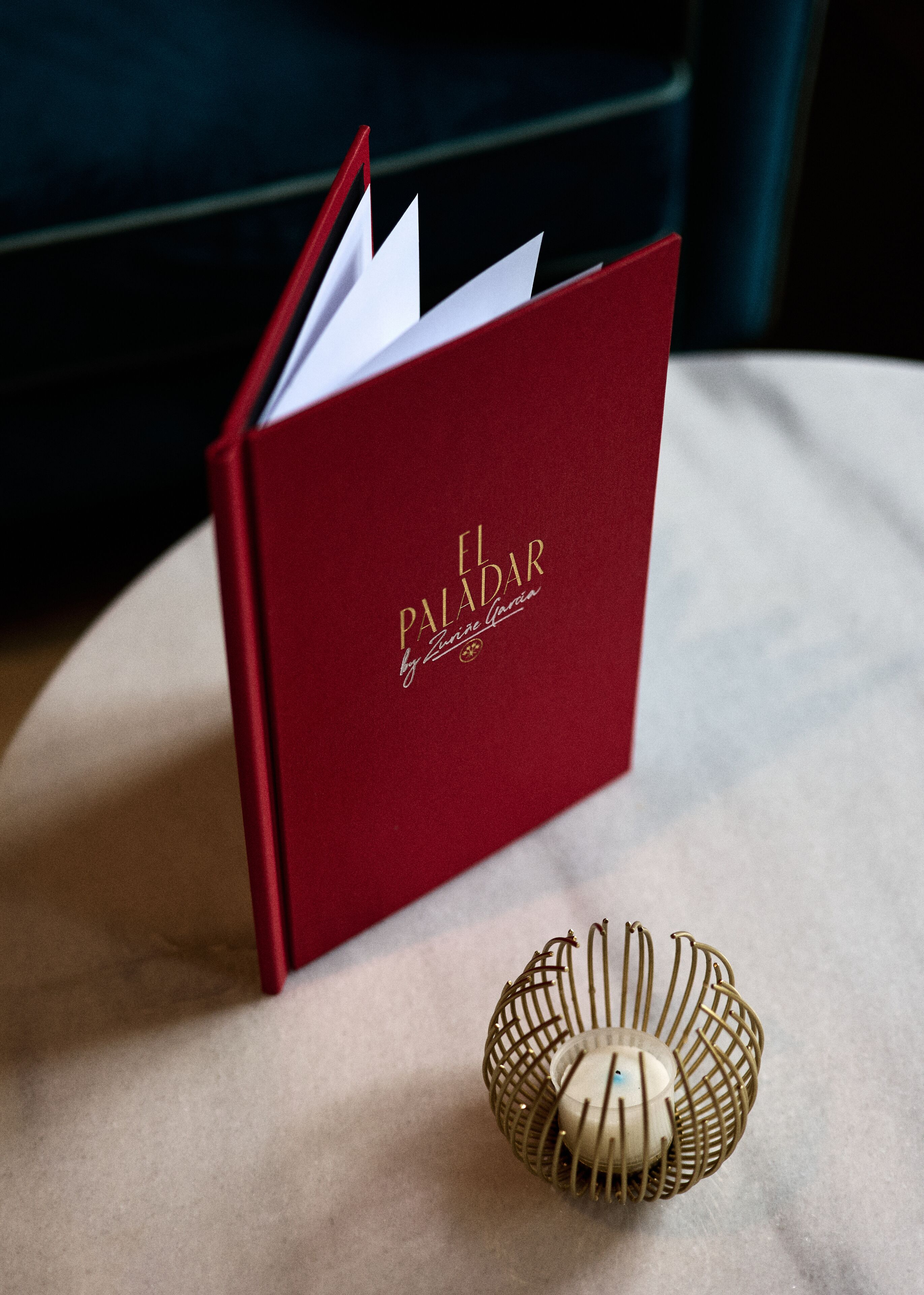 A red book titled "El Paladar" by Anne Garcia on a table next to a decorative candle holder.