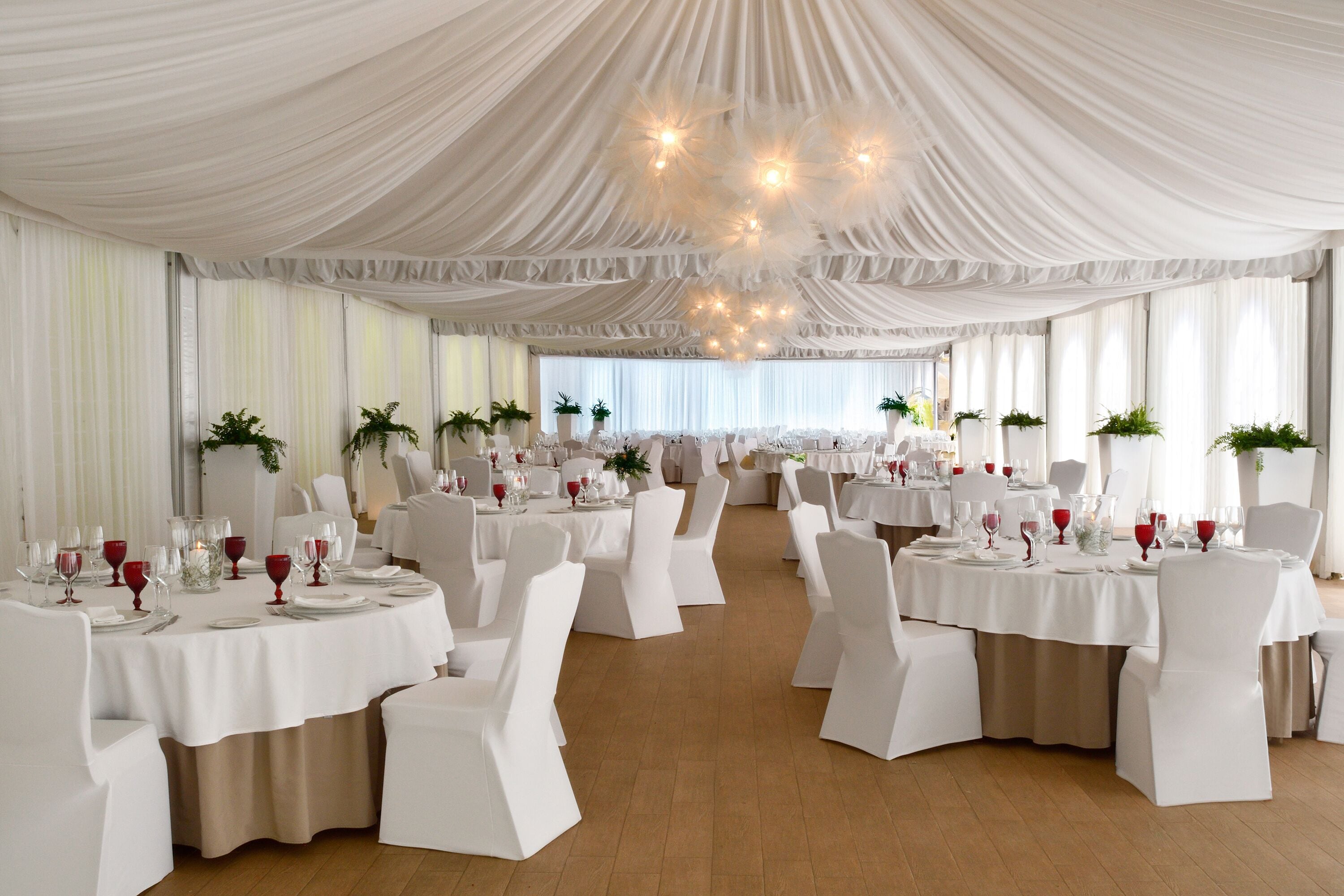 Un salón de banquetes con mesas redondas, sillas blancas y techos decorados con telas.
