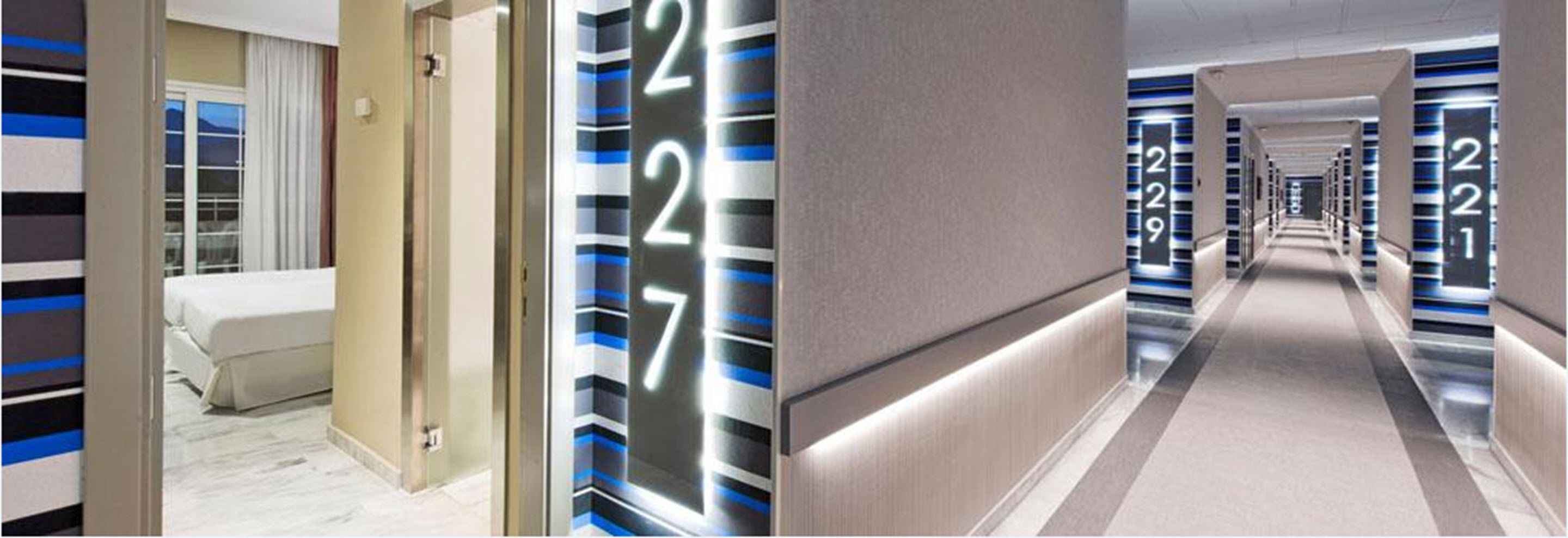 Un pasillo de hotel de diseño moderno, con un largo recorrido de puertas numeradas y suelo alfombrado.