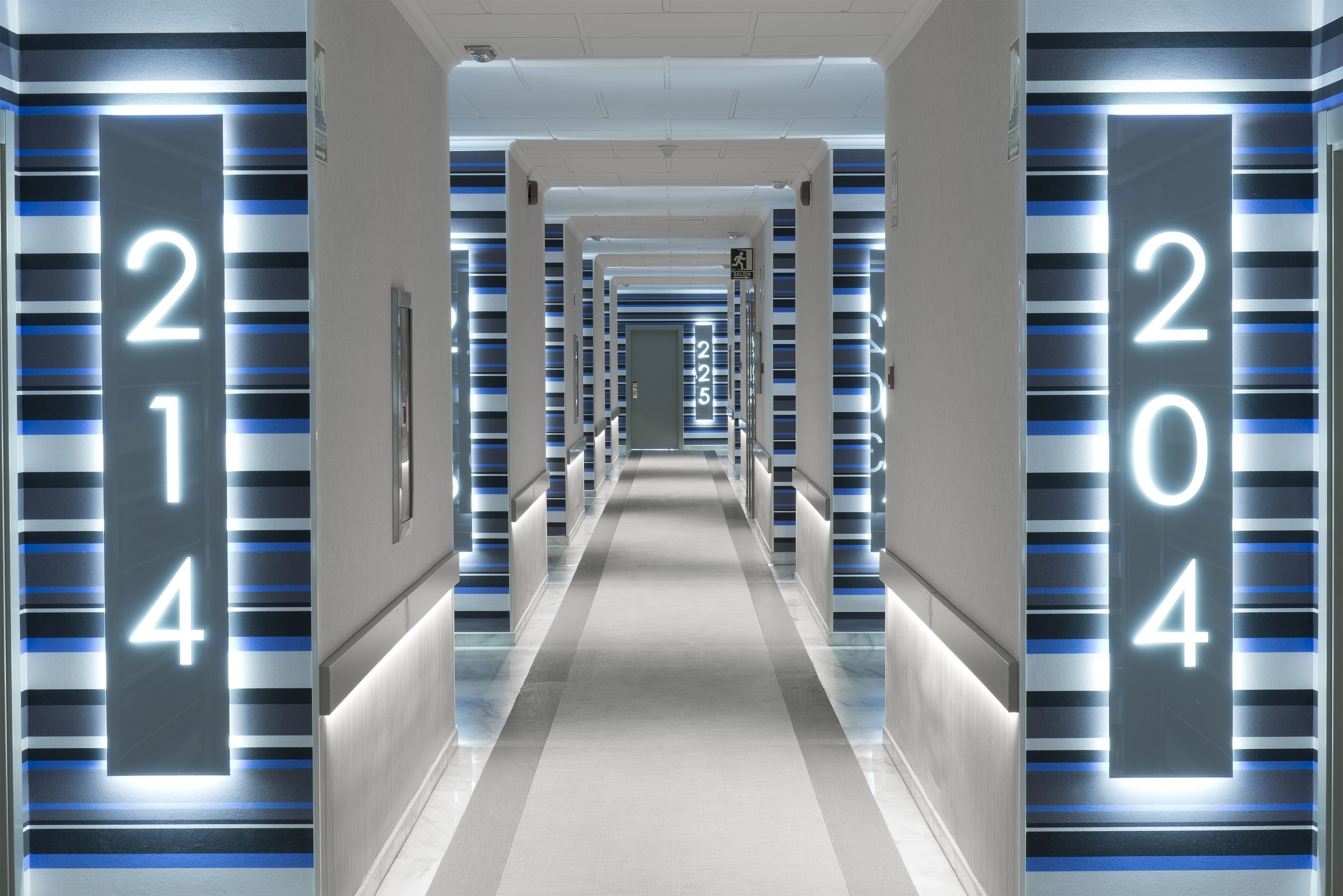 A modern hotel corridor with illuminated room numbers on the walls.