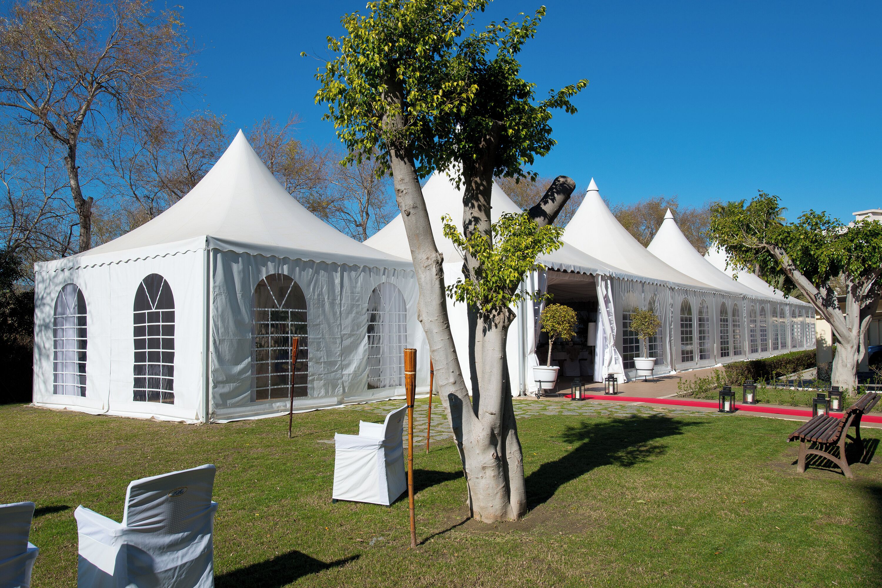 A row of white tents with arched windows, arranged in a line on a grassy field.