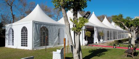 A row of white tents with arched windows, arranged in a line on a grassy field.