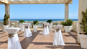 An outdoor terrace with white tables and chairs, potted plants, and a view of the ocean. - Elba Motril Beach & Business Resort (Motril)