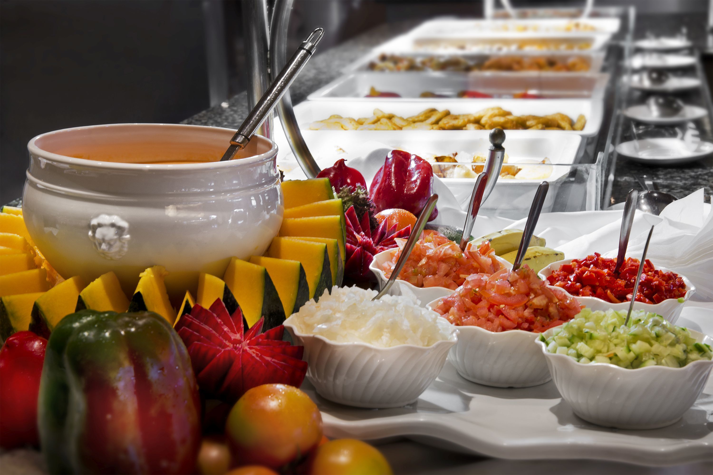 Un bufé con diversas opciones de comida, incluyendo frutas, verduras y salsas.