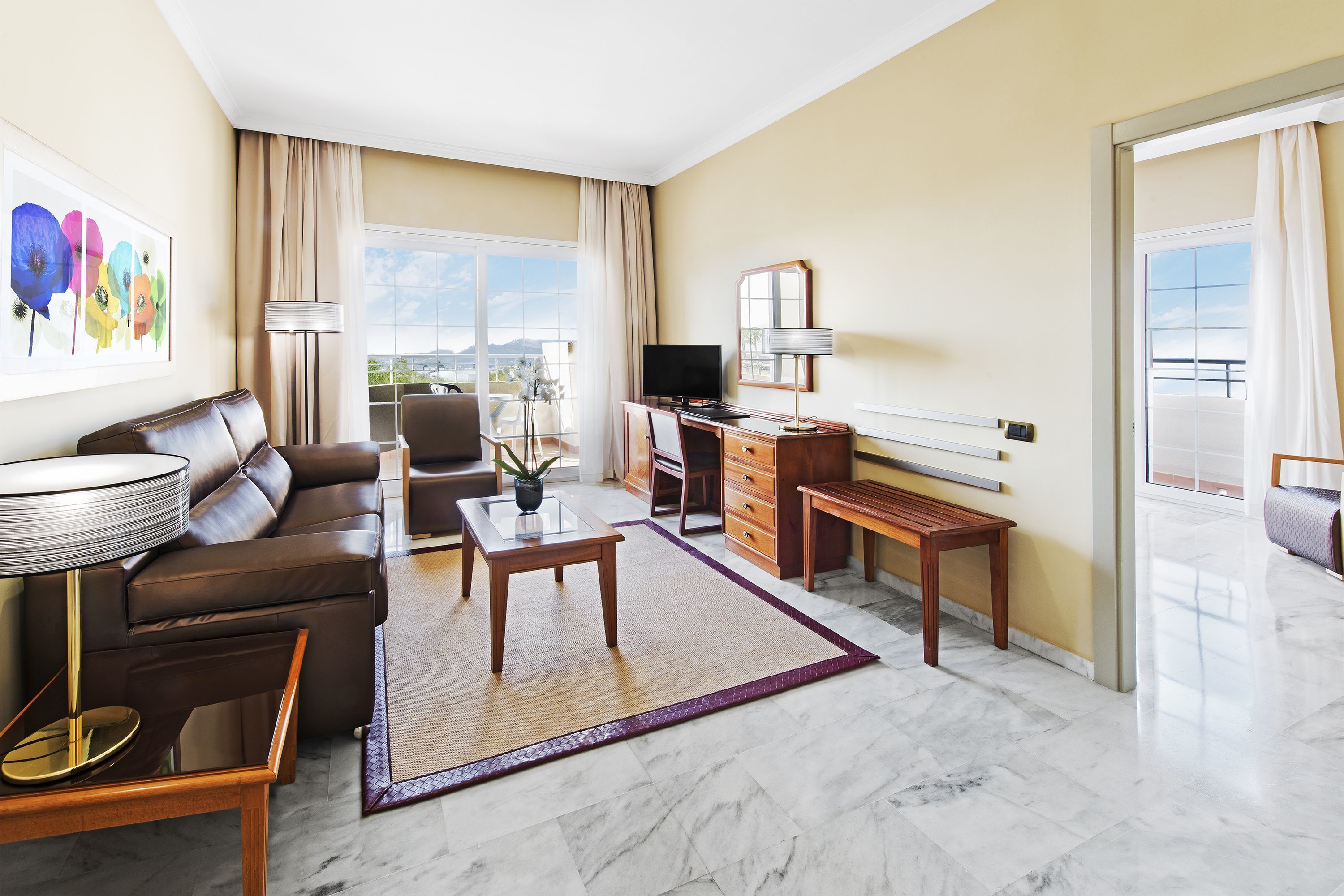 A modern living room with a sofa, a coffee table, a TV, and a balcony with a view.