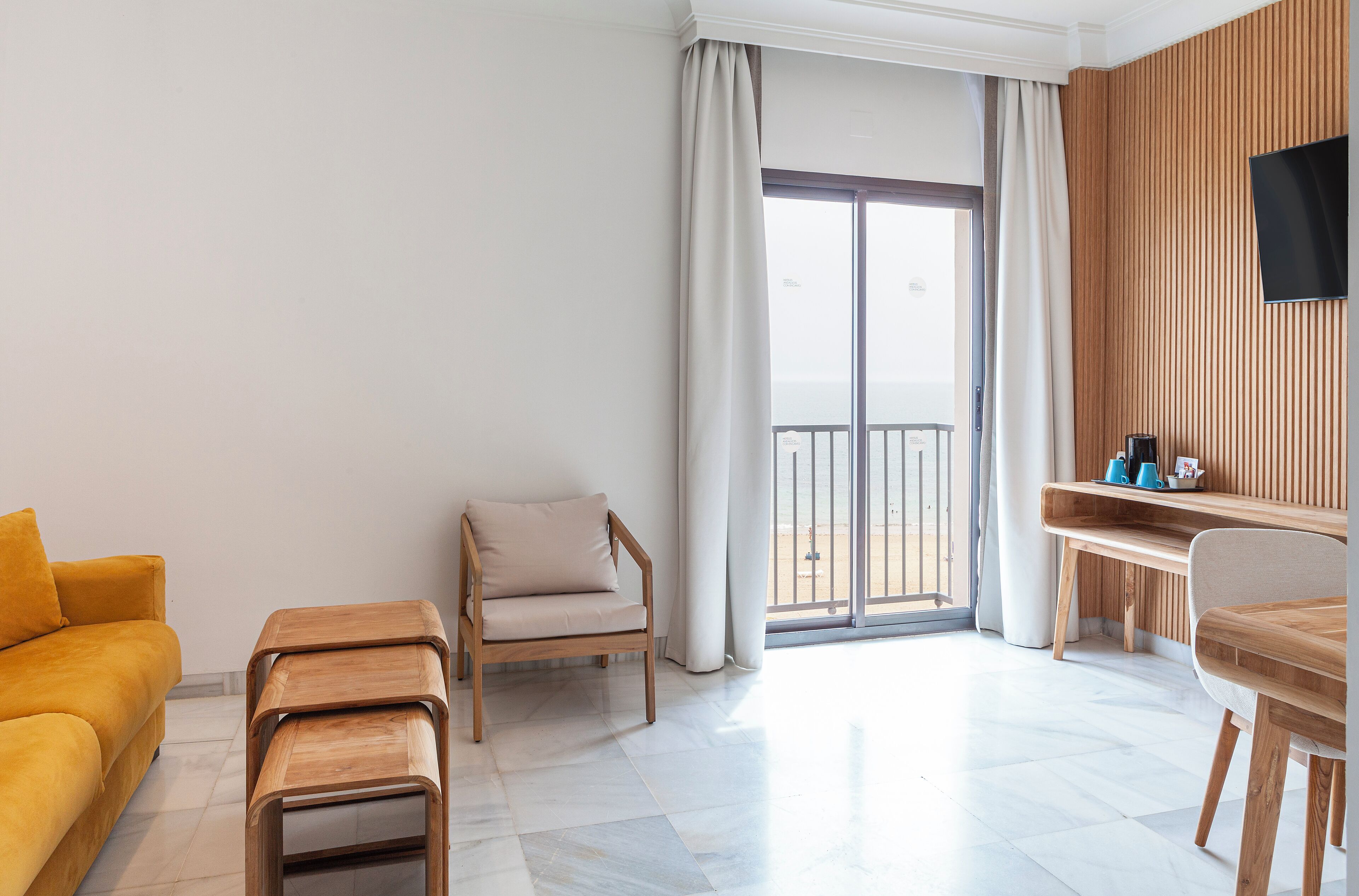 Una sala de estar moderna con un sofá, una silla de madera, una mesita y un televisor montado en la pared.