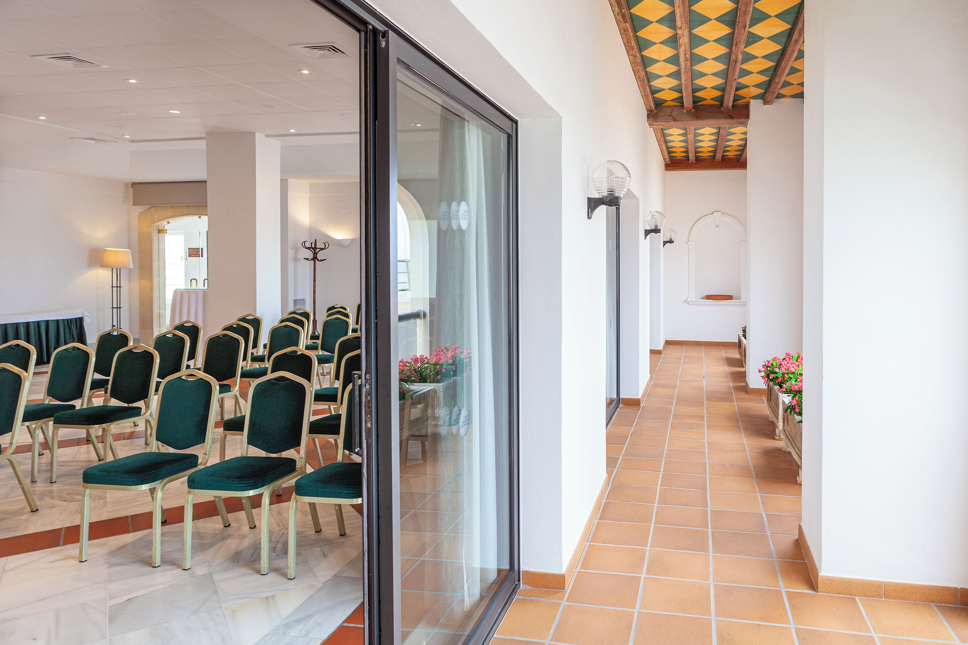 A conference room with rows of chairs, a glass partition, and a tiled floor.