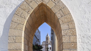 An arched stone passageway leading to a building with a bell tower. - Hotel Duque De Najera (Rota)