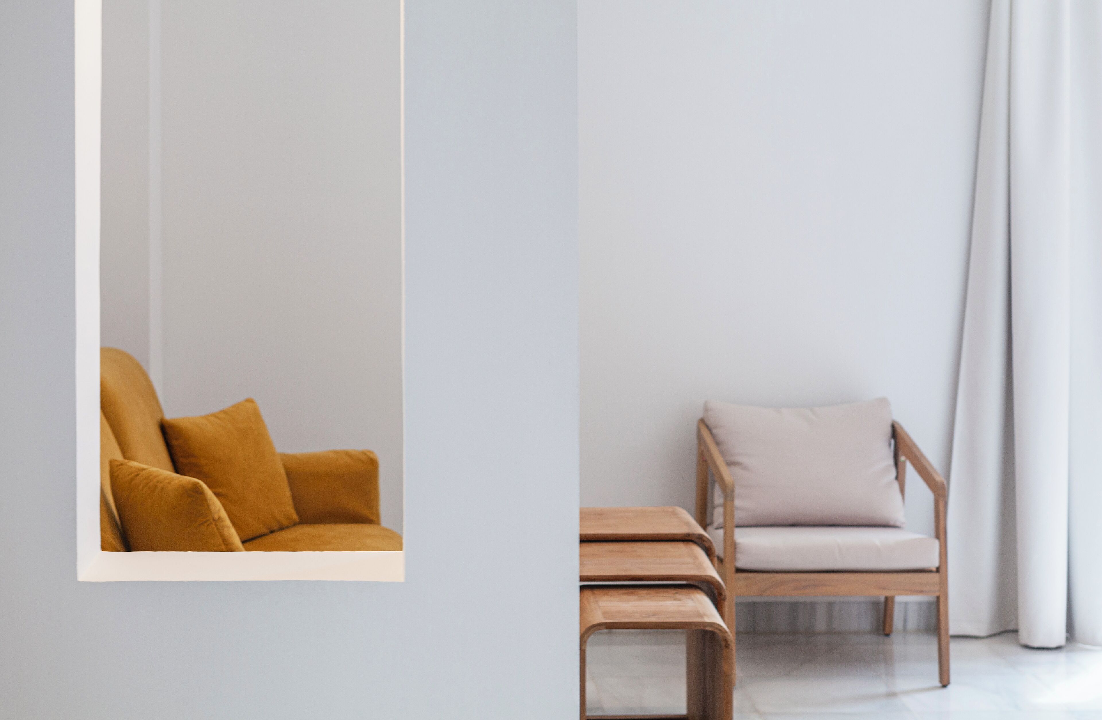 A room with a mustard-colored sofa and a light-colored chair with a wooden side table.