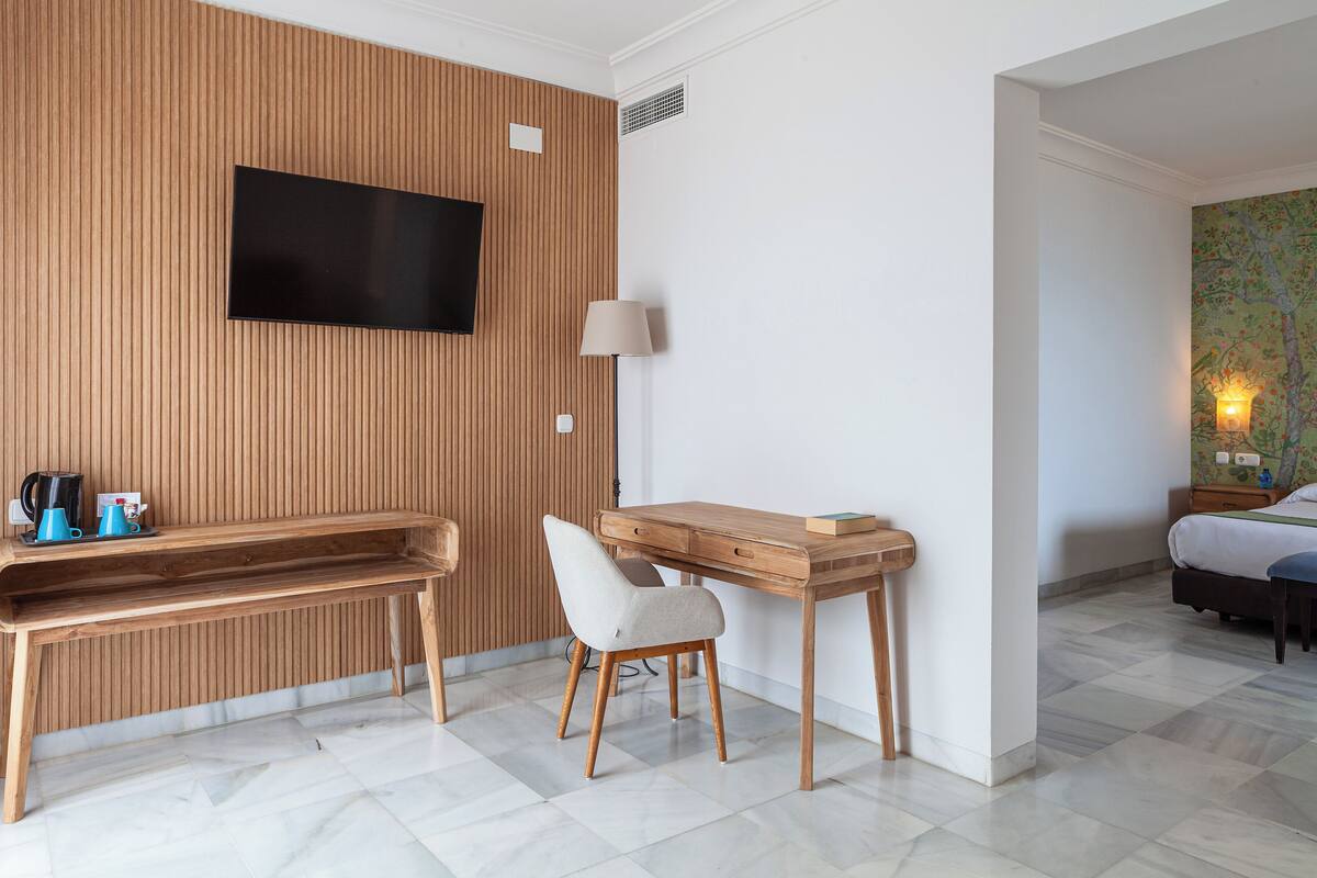 Habitación de hotel con pared de paneles de madera, televisor de pantalla plana, escritorio con silla, mesita de noche y cama.
