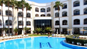 A pool with lounge chairs and palm trees, surrounded by a multi-story building with balconies. - Hotel Duque De Najera (Rota)