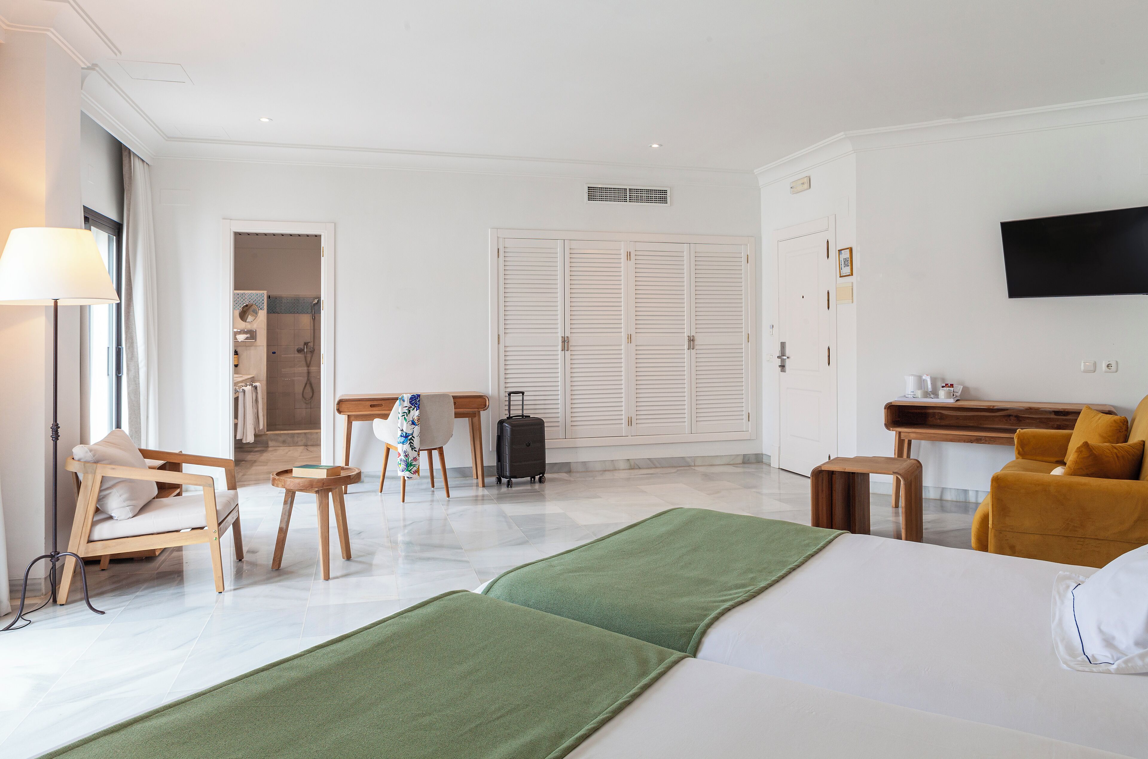 A hotel room with a bed, a desk, a chair, a lamp, and a TV.
