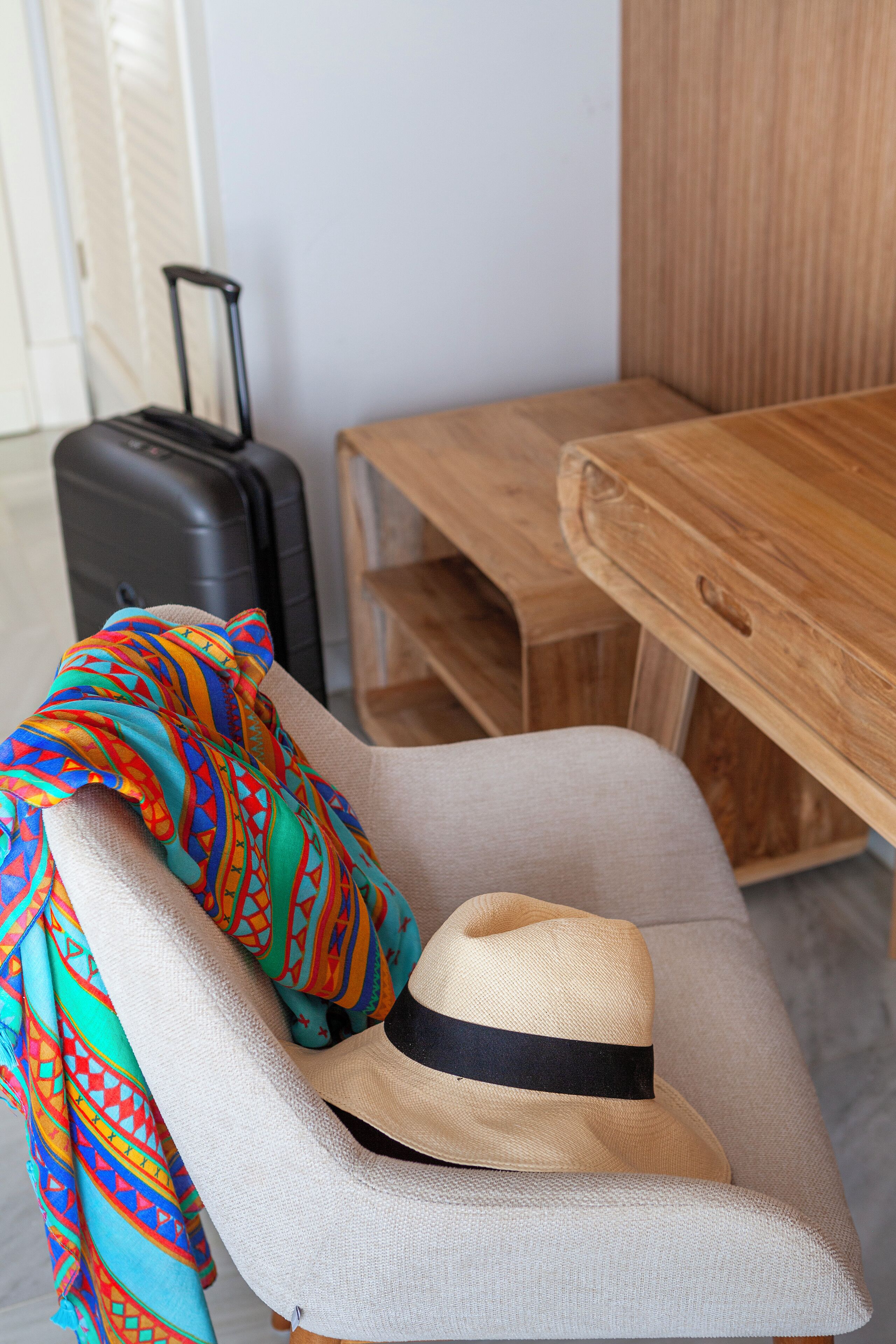 A chair with a suitcase and a colorful scarf, a wooden table, and a hat.