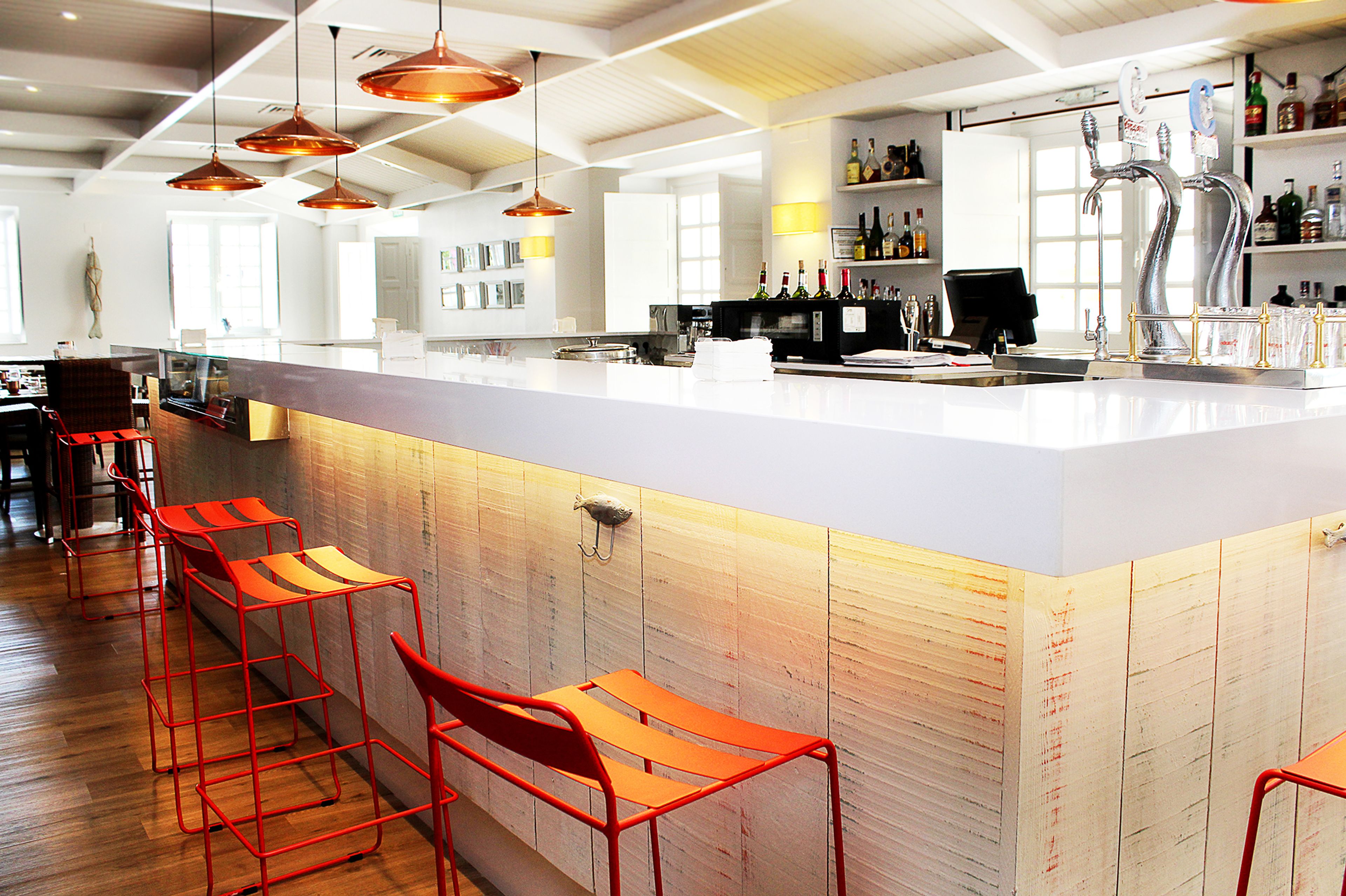 Zona de bar moderna con una barra alargada, taburetes rojos y una variedad de botellas de licor en estantes.