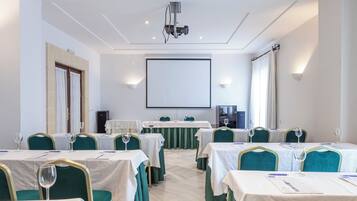 Un salón de conferencias con mesas dispuestas para una reunión, un proyector y una pantalla.