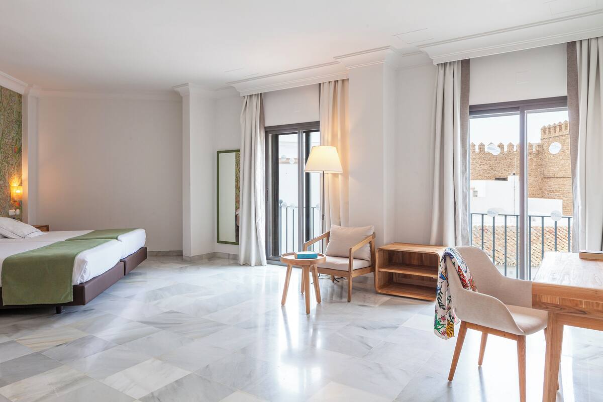 Habitación de hotel con cama, escritorio, silla, lámpara y vista a un edificio desde la ventana.