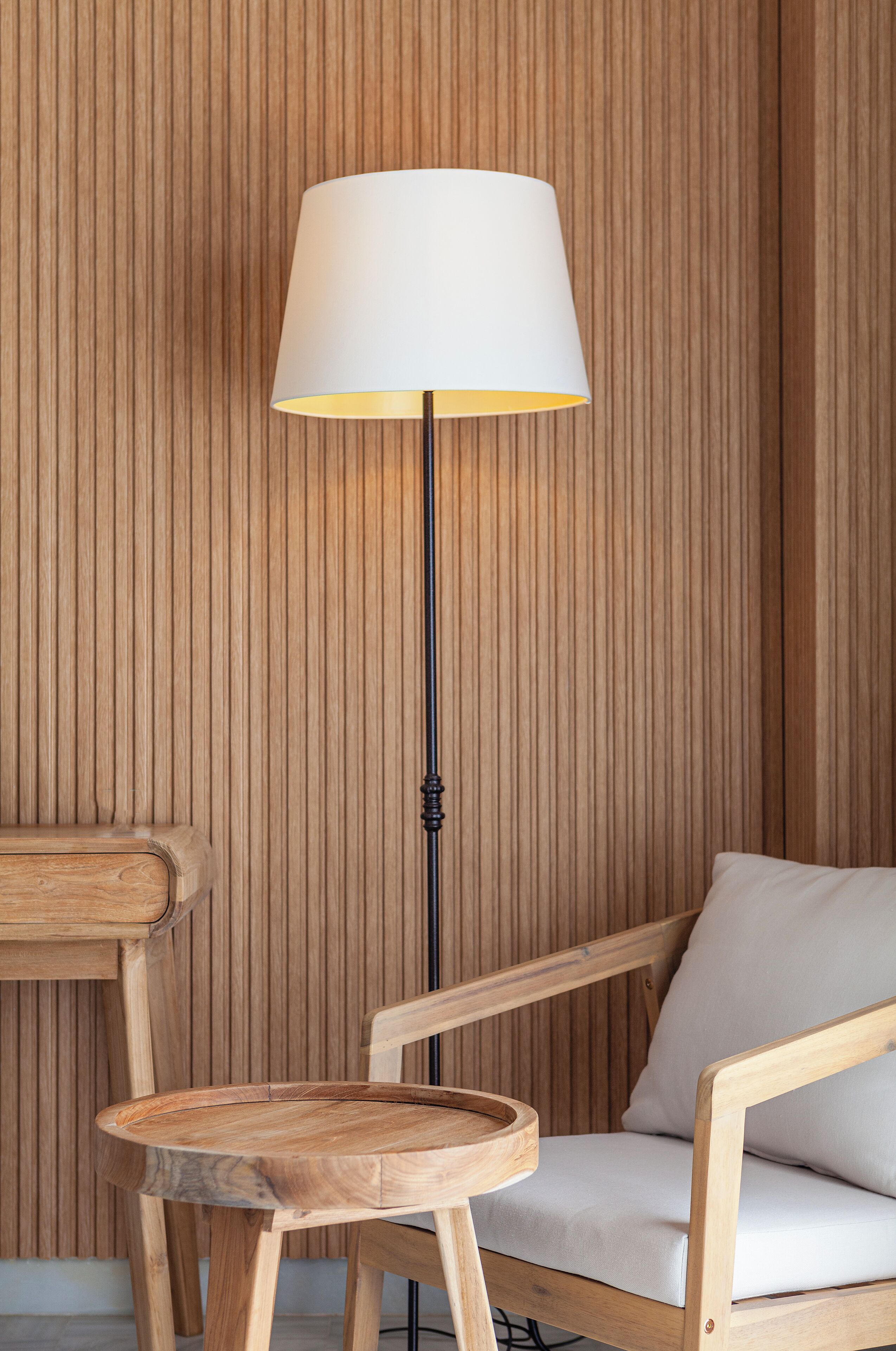 Un lampadaire en bois avec un abat-jour blanc, une chaise en bois avec un coussin et une petite table en bois.